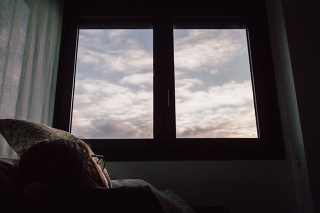 Žena s okuliarmi ležiaca pod veľkým oknom s výhľadom na oblohu.jpg